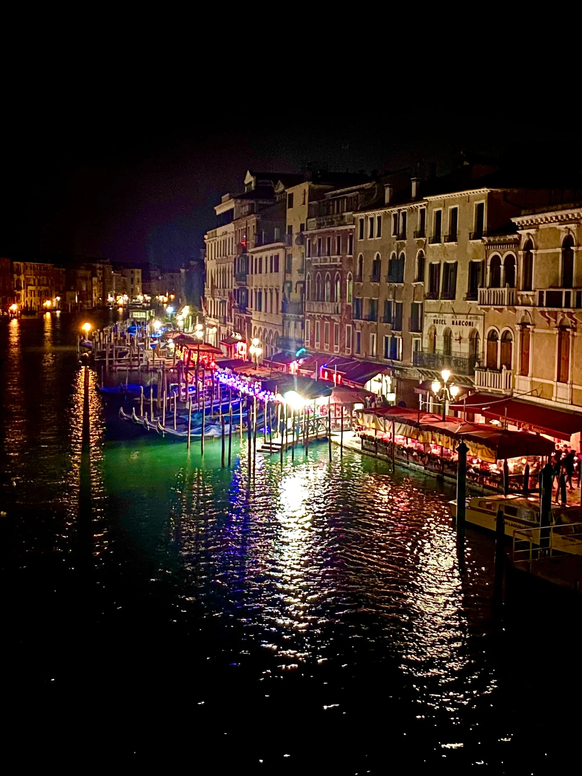 The Grand Canal in Venice lit up at night, with gondolas moored along the waterfront restaurants